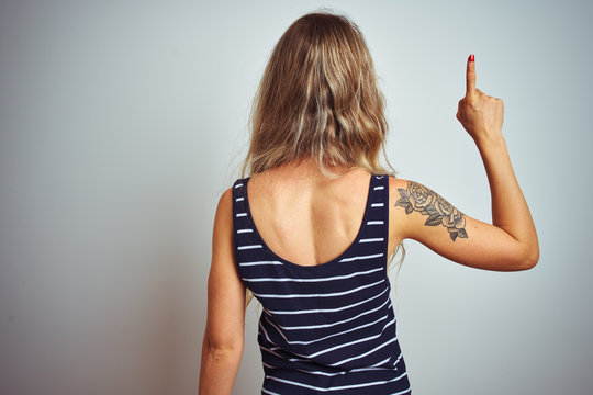 Young beautiful woman wearing stripes t-shirt standing over white isolated background Posing backwards pointing ahead with finger hand