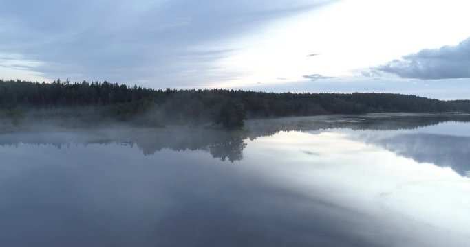 Aerial drone shot of a misty and calm lake before sunrise.