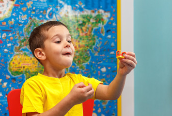 Little kid boy in yellow t-shirt playing with lots of colorful plastic blocks indoor. Child having fun with building and creating