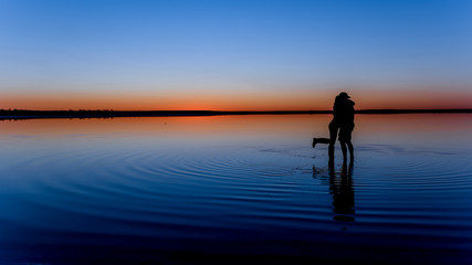Fototapeta premium Sihouette of man and woman hugging in watert at Lake Tyrrell at Sunset