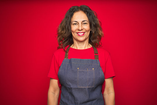 Middle age senior woman wearing apron uniform over red isolated background with a happy and cool smile on face. Lucky person.