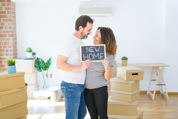 Fototapeta na wymiar Middle age senior couple moving to a new house, smiling happy in love with apartmant holding a blackboard with new home text