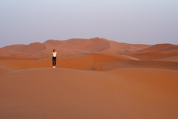 Traveler girl joyfully raises her hands on the top of the dune in Sahara desert, vacation in Morocco.