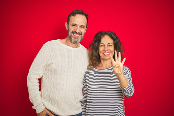 Naklejka premium Beautiful middle age couple wearing winter sweater over isolated red background showing and pointing up with fingers number four while smiling confident and happy.