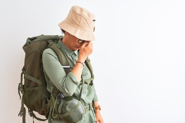 Fototapeta premium Middle age hiker woman wearing backpack canteen hat glasses over isolated white background tired rubbing nose and eyes feeling fatigue and headache. Stress and frustration concept.