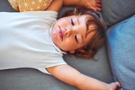 Beautiful toddler child girl wearing white bodysuit lying down on the sofa