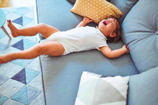 Beautiful toddler child girl wearing white bodysuit crying lying down on the sofa