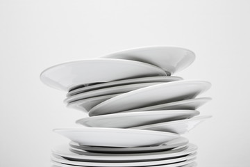 Messy stack of white plates about to fall, isolated on white