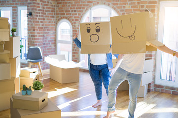 Crazy couple wearing cardboard boxes with funny emoji faces over head, having fun at new house