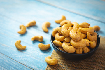 Top view of roasted cashew nut in salt in black bowl  on soft blue vintage wood table