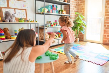 Beautiful teacher and blond student toddler girl playing with plastic frogs toys at kindergarten