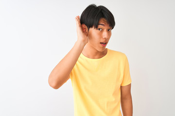 Chinese man wearing yellow casual t-shirt standing over isolated white background smiling with hand over ear listening an hearing to rumor or gossip. Deafness concept.