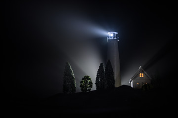 Fototapeta na wymiar Lighthouse with light beam at night with fog. Old lighthouse standing on mountain. Table decoration. Toned background. Moonlighting.