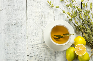 White cup of herbal sage tea with dried sage leaves and lemon on white wooden rustic background. Herbal tea hot drink concept,  Salvia officinalis