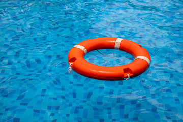 Plastic orange lifebuoy on blue water of swimming pool. Safety on water concept. Kids swimming lesson equipment.