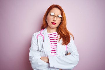 Young redhead doctor woman wearing glasses over pink isolated background skeptic and nervous,...