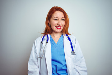 Young redhead doctor woman using stethoscope over white isolated background winking looking at the camera with sexy expression, cheerful and happy face.