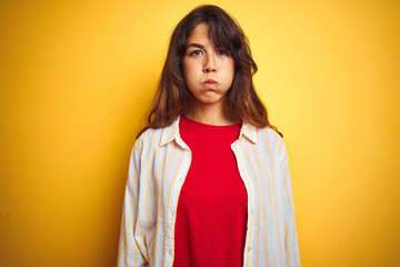 Young beautiful woman wearing red t-shirt and stripes shirt over yellow isolated background puffing cheeks with funny face. Mouth inflated with air, crazy expression.
