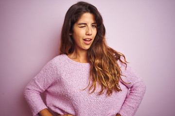 Young beautiful woman wearing sweater standing over pink isolated background winking looking at the camera with sexy expression, cheerful and happy face.