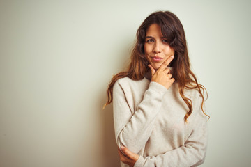 Young beautiful woman wearing winter sweater standing over white isolated background looking confident at the camera smiling with crossed arms and hand raised on chin. Thinking positive.