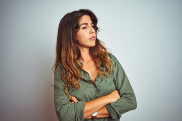 Young beautiful woman wearing green shirt standing over grey isolated background looking to the side with arms crossed convinced and confident