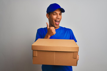 Young handsome arab delivery man holding a box standing over isolated white background happy with big smile doing ok sign, thumb up with fingers, excellent sign