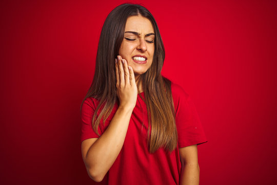 Young beautiful woman wearing t-shirt standing over isolated red background touching mouth with hand with painful expression because of toothache or dental illness on teeth. Dentist concept.