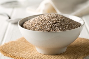 Whole, organic white chia seeds heap in white bowl with bright kitchen background - selective focus