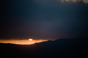 Dramatic cloudy sunset with sun disk peeking out of clouds