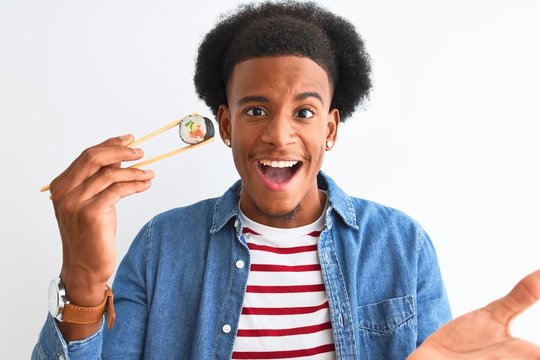 Young African American Man Eating Sushi Using Chopsticks Over Isolated White Background Very Happy And Excited, Winner Expression Celebrating Victory Screaming With Big Smile And Raised Hands