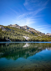 Wispy clouds over Shadow Lake in Eastern Sierra with pine forest and craggy mountains reflecting in lake