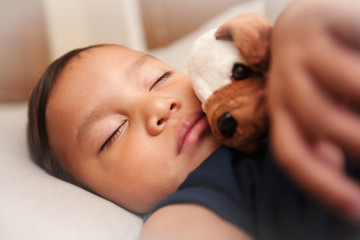 Obraz premium Little latino boy resting or dreaming and holding his plush toy next to his face.