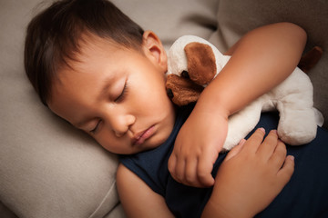 A young male child who fell sleep during the daytime while hugging his stuffed animal toy.