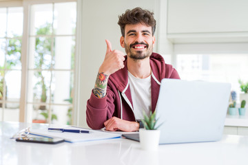 Young student man using computer laptop and notebook happy with big smile doing ok sign, thumb up...