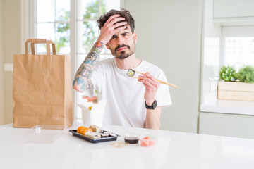 Young man eating asian sushi from home delivery stressed with hand on head, shocked with shame and surprise face, angry and frustrated. Fear and upset for mistake.