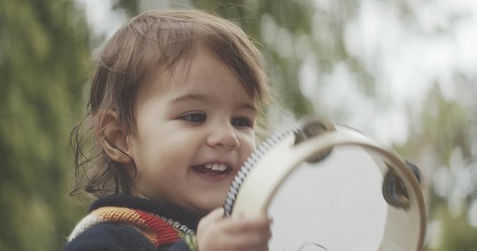 Cute baby girl playing a tambourine outdoors. Shot in 4K RAW on a cinema camera.