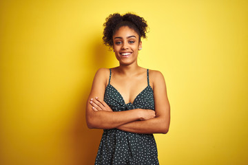 African american woman wearing summer casual green dress over isolated yellow background happy face smiling with crossed arms looking at the camera. Positive person.