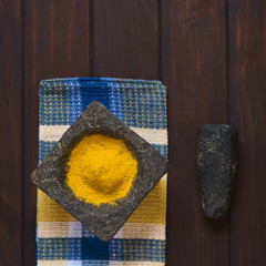 Overhead shot of curry powder spice in mortar with pestle on the side, photographed on dark wood with natural light