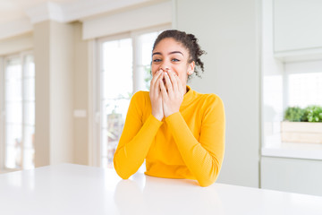 Beautiful african american woman with afro hair wearing a casual yellow sweater laughing and embarrassed giggle covering mouth with hands, gossip and scandal concept