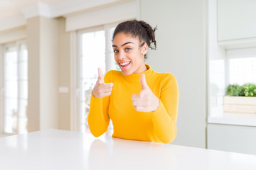 Fototapeta na wymiar Beautiful african american woman with afro hair wearing a casual yellow sweater pointing fingers to camera with happy and funny face. Good energy and vibes.