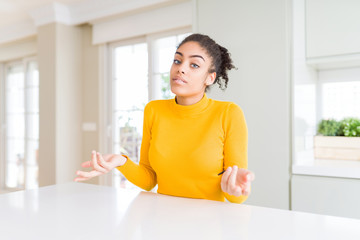 Beautiful african american woman with afro hair wearing a casual yellow sweater clueless and confused with open arms, no idea concept.