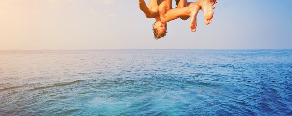 Young man jumping off cliff into blue water ocean at sunset. Active outdoor, holiday adventure, tourism action, healthy summer joy, Fun activity lifestyle. Crazy adult guy in swimwear fly from climb. - Powered by Adobe