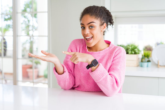 Beautiful african american woman with afro hair wearing casual pink sweater amazed and smiling to the camera while presenting with hand and pointing with finger.