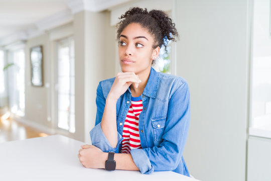 Beautiful young african american woman with afro hair wearing casual denim jacket with hand on chin thinking about question, pensive expression. Smiling with thoughtful face. Doubt concept.