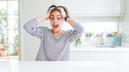 Beautiful african american woman with afro hair wearing casual striped sweater Crazy and scared with hands on head, afraid and surprised of shock with open mouth