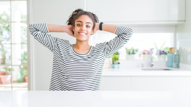 Beautiful african american woman with afro hair wearing casual striped sweater relaxing and stretching, arms and hands behind head and neck smiling happy