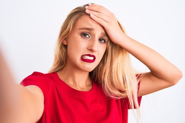 Fototapeta premium Young beautiful woman wearing t-shirt make selfie by camera over isolated white background stressed with hand on head, shocked with shame and surprise face, angry and frustrated. Fear and upset