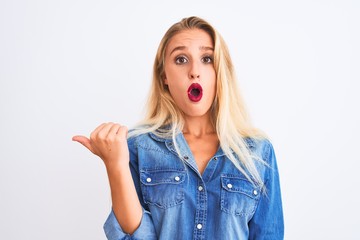 Young beautiful woman wearing casual denim shirt standing over isolated white background Surprised pointing with hand finger to the side, open mouth amazed expression.