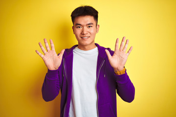 Young asian chinese man wearing purple sweatshirt standing over isolated yellow background showing and pointing up with fingers number ten while smiling confident and happy.