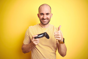 Young man playing video games using joystick gamepad over isolated yellow background happy with big smile doing ok sign, thumb up with fingers, excellent sign © Krakenimages.com